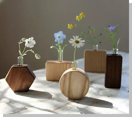 自然光が差し込む明るい室内で、木製の小さな一輪挿しが数種類並んでいる様子。丸や六角形など異なる形の木製ベースに、可憐な野花が活けられ、生活の中での使用シーンをイメージさせる写真。